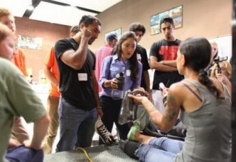 Army sergeant sits on the stage and shows design students the components of her prosthetic leg.